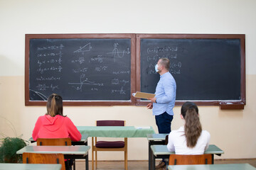 Students in protective face masks studying in classroom with teacher. Precautions in coronavirus pandemic