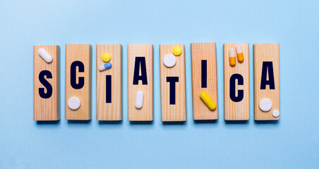 Fototapeta na wymiar The word SCIATICA is written on wooden blocks on a light blue table near the pills. Medical concept