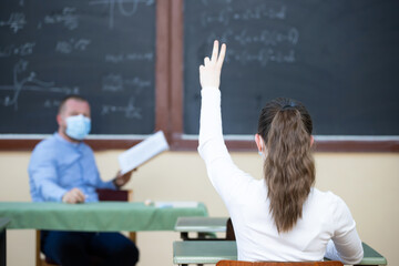 Students in protective face masks studying in classroom with teacher. Precautions in coronavirus...