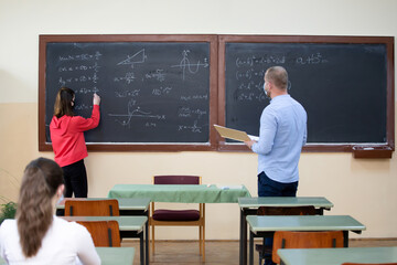 Students in protective face masks studying in classroom with teacher. Precautions in coronavirus pandemic