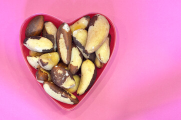 Brazilian nuts in the shape of a heart on a pink background, top view. Healthy food brazil nut, vegan product concept