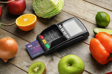 Payment terminal with credit card and food on wooden background