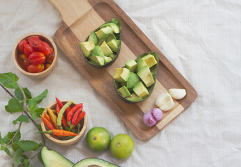 Sliced avocado,shallot and garlic put on wooden tray beside tomato,chili and lime.