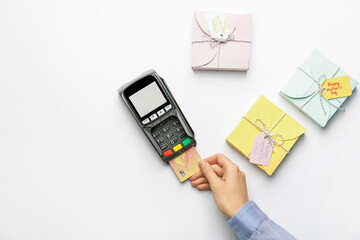 Female hand with credit card, payment terminal and gift boxes on white background