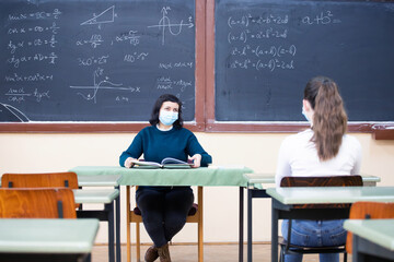 Students in protective face masks studying in classroom with teacher. Precautions in coronavirus pandemic