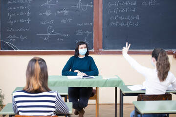 Students in protective face masks studying in classroom with teacher. Precautions in coronavirus pandemic