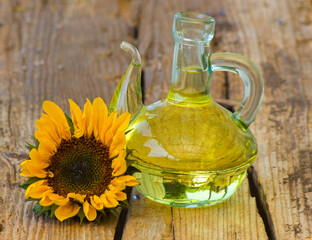 Glass bottle with sunflower oil and sunflower on wooden background