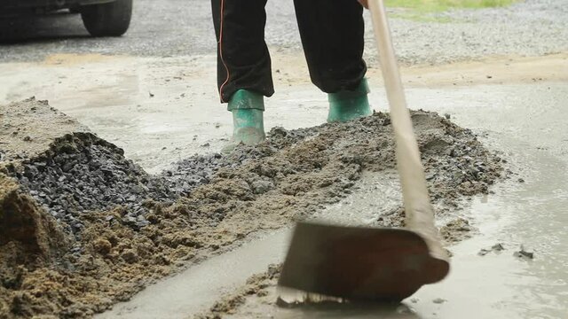 Asian workers mixing concrete with cement, aggregate and sand with a shovel at construction site.