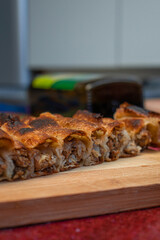 homemade Bosnian pie burek with meat in a traditionally made vessel and old homemade Persian style rug and wooden plate