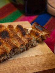 homemade Bosnian pie burek with meat in a traditionally made vessel and old homemade Persian style rug and wooden plate