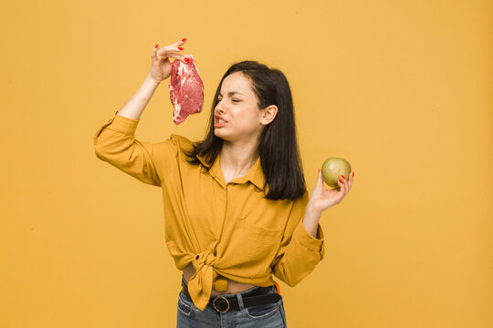 Concept photo of sweet vegetarian female is smelling meat and looks she doesn t like it. Wears yellow shirt, isolated yellow color background