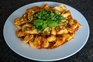 ready to eat, homemade tortelloni stuffed with prosciutto in tomato sauce with basil