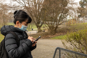 Japanese woman using medical mask looking to the smartphone in German park