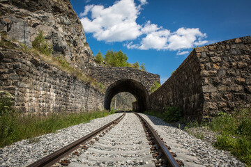 Circum-Baikal Railway. Tunnel and powerful fencing walls. Railway rails in the foreground. Summer sunny day, blue sky.