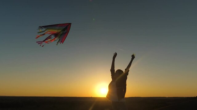 A happy girl runs with a kite in her hands across field in rays of the sunset. A healthy child dreams of freedom, flight. Kid plays outdoors in the park. Teen wants to be a pilot