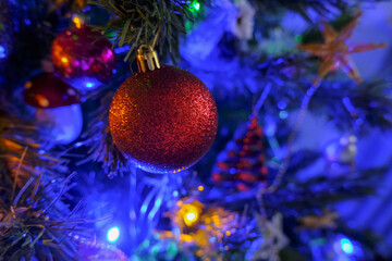 Obraz na płótnie Canvas red shining ball with golden details hanging on Christmas tree across other decorations close-up. Christmas decoration on a tree. Holidays decor. Christmas card