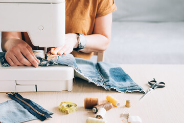 A woman tailor works at sewing machine sews reuses fabric from old denim clothes