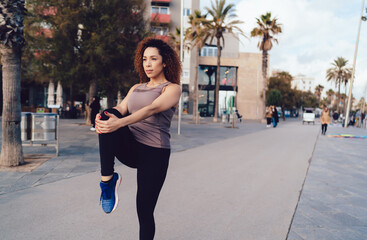 Confident young ethnic woman stretching on street