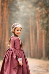 Little cute girl in a historical dress is walking in a pine forest