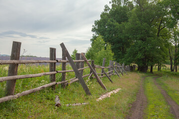 Summer landscape with cloudy sky and old fence near the countryside road