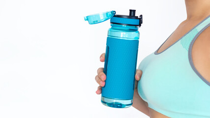 Sports blue water bottle in the hand of a toned tanned slender young woman in a turquoise short top isolated on white background. Fitness concept, healthy lifestyle. Copy space for design