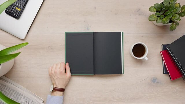 Above shot of businessman reading blank book page, closing book, putting down his black fountain pen and taking a coffee break. Top view of light wooden table with books, daylight, 4k Close-up