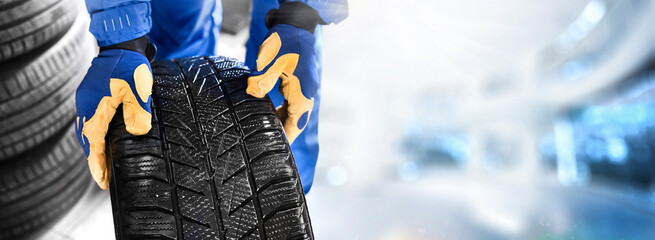 Mechanic holding tire with copy space for text repair service center, blurred background, - obrazy, fototapety, plakaty