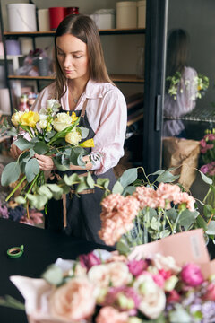 Photo of successful modern florist wearing apron making picture of flower, creating beautiful bouquet of colorful different flowers in modern interior floral shop