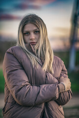 Portrait of a young beautiful blonde girl in a gray jacket outdoors.