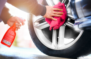 Car detailing close up. Man holds red microfiber in hand and polishes the wheel alloy tire.