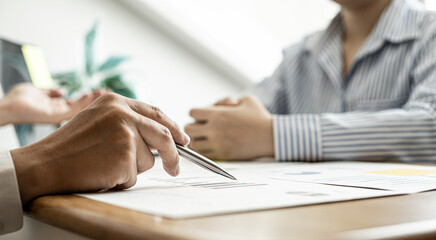 A close-up of a financial businessman holding a pen and pointing at the information sheet on his desk, reading the company's financials to make a financial plan. Financial concept.