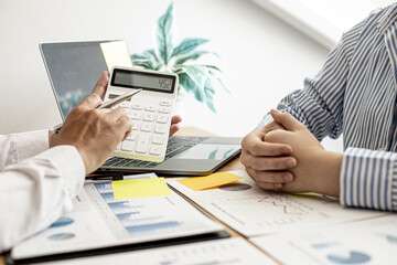 A business man using a calculator to check company financial information Together with business partners, they are having a brainstorming meeting planning to grow the company. Financial concept.
