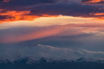 Fototapeta na wymiar Bright sunset with orange clouds. Panoramic view on the mountain peak snow-covered on the sunset.