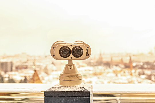 Coin-operated binoculars on the observation deck overlooking the city from a height at sunset. Winter, snowfall.