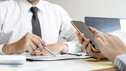 Business woman is using a smartphone to check the financial data of the company Together with business partners, they are having a brainstorming meeting planning to grow the company. Financial concept