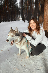 Cute girl in a winter park. Woman palying with a dog. Girl in white hoodie plays with husky