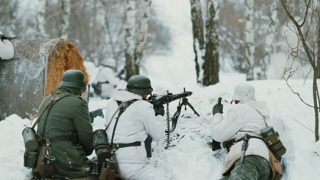 Men Dressed As German Wehrmacht Infantry Soldiers In World War II Hidden Sitting With Weapon In An Ambush And Aiming a Machine Gun at Enemy From Trench In Winter Day. Slow Motion