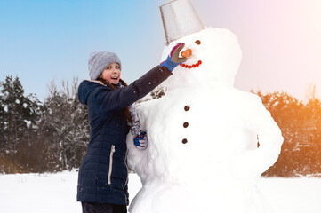 Cute girl makes  snowman on  winter day. Girl on a snow-covered field in the open air. Artistically...