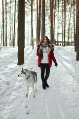 Fototapeta na wymiar Cute girl in a winter park. A woman plays with a dog. Girl in a red jacket with a hood plays with a husky