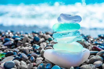Sea glass stones arranged in a balance pyramid on the beach. Beautiful azure color sea with blurred seascape background. Meditation and Harmony concept.