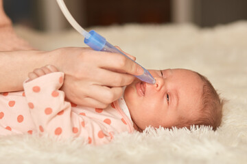 Faceless person using nasal aspiration sucks the snot from baby, infant lying on bed, looks...