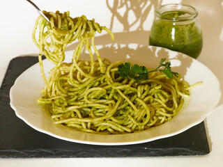 Male having a Delicious Spaghetti with pesto sauce and a parsley leaf and the image is decorated with a glass of Pesto Sauce