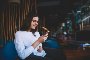 Positive young woman browsing mobile in cafe