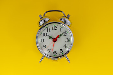 old mechanical alarm clock lies on a yellow background.