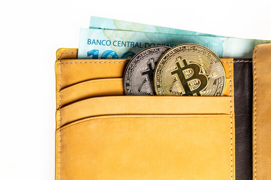 Carteira de couro com criptomoedas Bitcoin e c&eacute;dulas de dinheiro isolada em fundo branco. Notas de cem Reais.