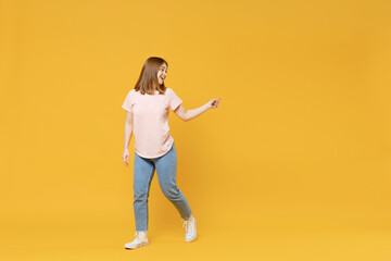 Full length of young caucasian woman 20s wearing casual basic pastel pink t-shirt, jeans pointing index finger aside on workspace area mock up copy space isolated on yellow background studio portrait.