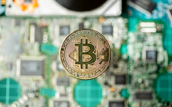 Token de criptomoeda Bitcoin dourada em foco em cima de placas eletr&ocirc;nicas e pe&ccedil;as de computador com um disco r&iacute;gido aberto desfocados em plano de fundo. Visto de cima.