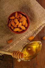 Almonds in a bowl on sacking next to honey with a spoon on a wooden table.