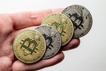 Mão segurando tokens de criptomoedas Bitcoin douradas e prateadas com plano de fundo desfocado.
