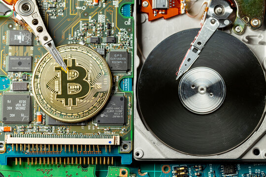 Token de criptomoeda Bitcoin dourada em cima de placas eletr&ocirc;nicas e pe&ccedil;as de computador com um disco r&iacute;gido aberto. Visto de cima.